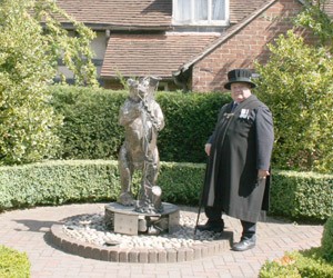 A Bailif in uniform, stood next to a statue of the Warwickshire Bear & ragged staff